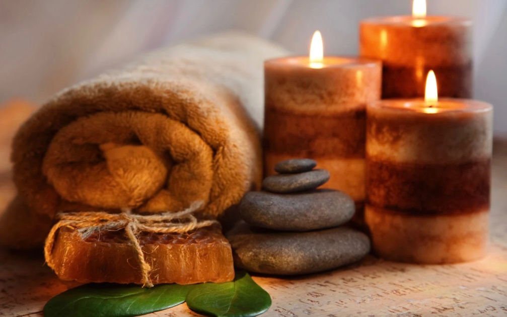Candles glowing beside a rolled towel, smooth stacked stones and a bar of honey soap