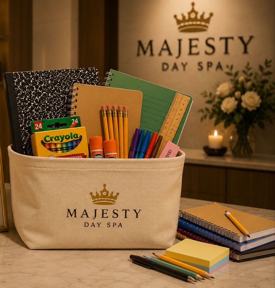 A canvas basket with a gold Majesty Day Spa crown logo, filled with notebooks, pencils, markers, crayons and glue sticks on the spa's front desk
